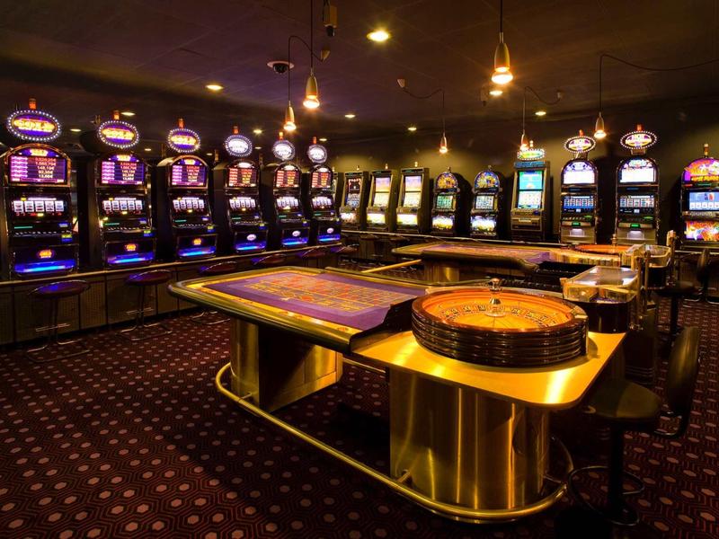 Vue d'une salle de casino avec des machines à sous et des tables de jeu sous un éclairage tamisé