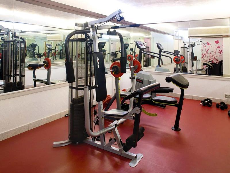 Salle de sport avec appareils sur sol rouge et grands miroirs au mur.