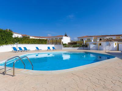 Runder Außenpool mit blauen Liegestühlen und weißen Gebäuden bei klarem Himmel.