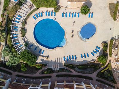 Luftaufnahme eines Hotelpools mit zwei Becken und Liegestühlen auf dem umliegenden Patio.