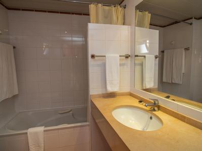 Kleines Badezimmer mit weißer Badewanne, beigem Waschtisch und großen Spiegeln an der Wand.