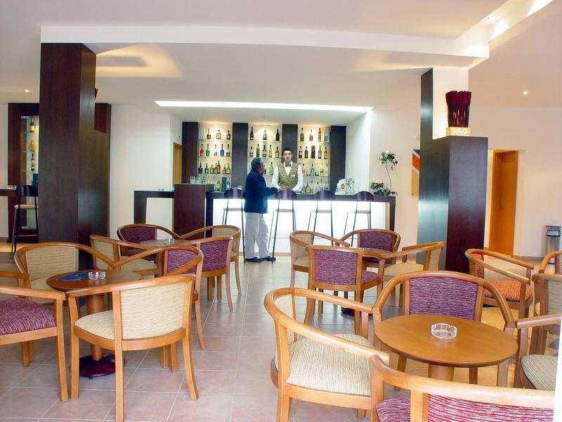 Heller Barraum mit Holzstühlen, Glastischen und beleuchtetem Tresen im Hintergrund.