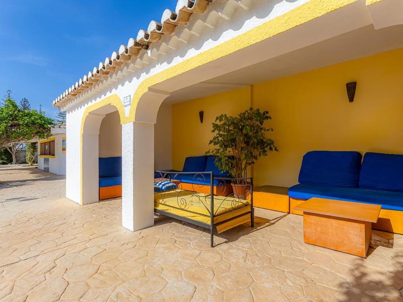 Sonnige Terrasse mit gemütlicher Sitzgruppe und blauem Polster vor gelber Wand.