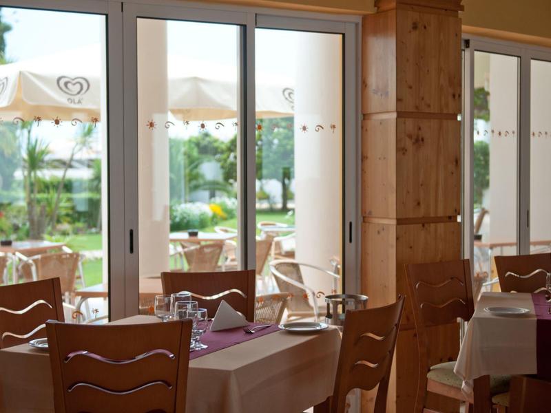 Helles Restaurant mit Holzmöbeln, gedeckten Tischen und großen Fenstern zum Garten mit Sonnenschirmen.