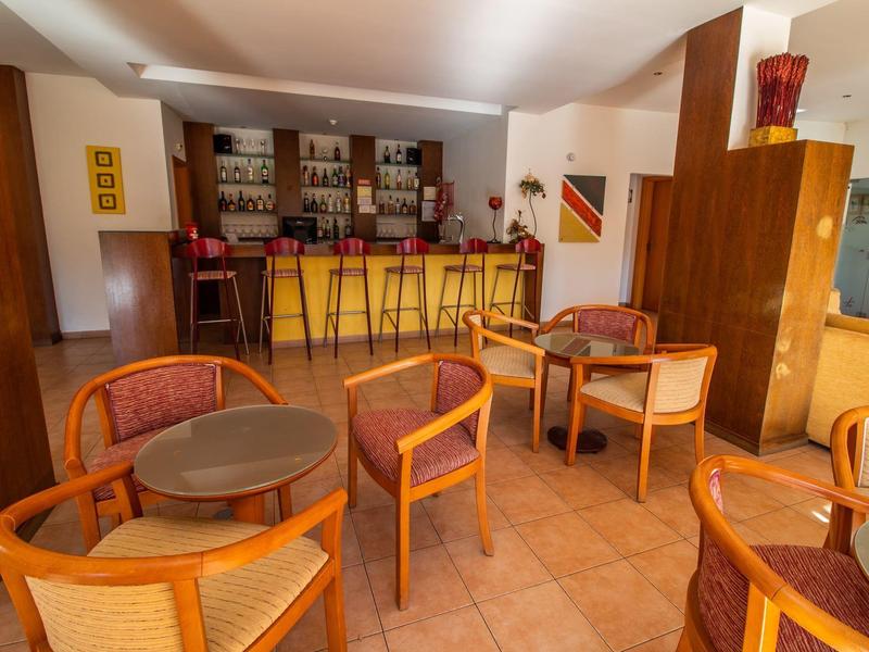 Gemütliche Bar mit Holzmöbeln, runden Tischen und warmem Licht, helle Fliesen und dekorative Regale.