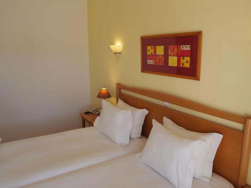 Einfach eingerichtetes Schlafzimmer mit zwei Einzelbetten, Kissen und einem Bild an der Wand.