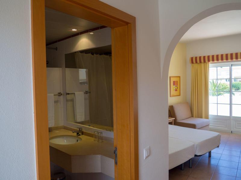 Innenraum mit Blick auf ein Badezimmer links und ein Wohnzimmer mit Sofa und großen Fenstern rechts.