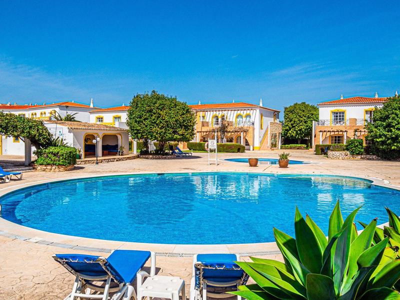 Großer runder Pool mit blauer Liege, umgeben von weißen Häusern und grünem Pflanzenbesatz.