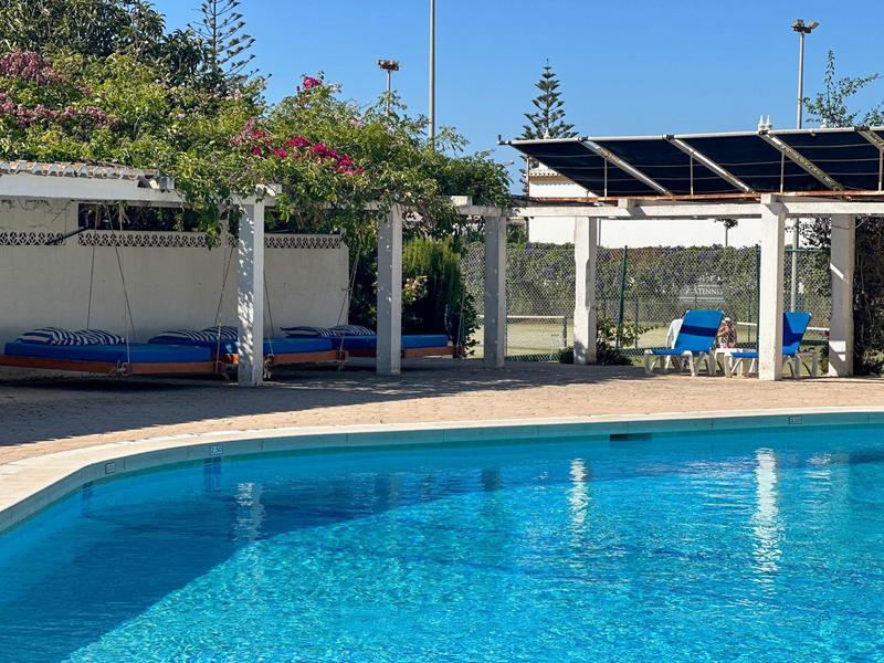 Schwimmbad mit klarem blauen Wasser, überdachte Sitzecke und bunte Pflanzen am Rand.