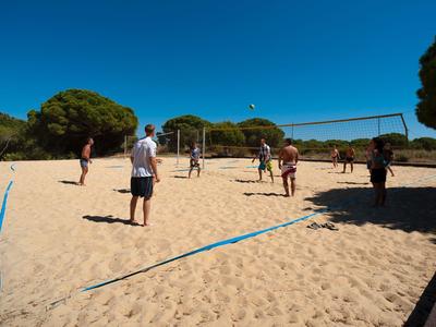 People playing volleyball on a sand court under a clear blue sky.