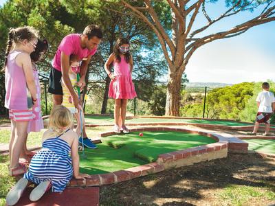 Children playing mini golf on a sunny, green outdoor course.