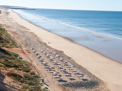 Lunga spiaggia di sabbia con lettini e mare blu sotto un cielo sereno.
