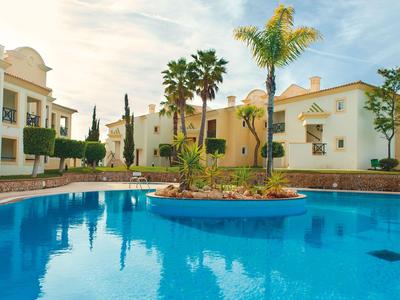 Blue swimming pool with palm trees and white apartments in sunlight