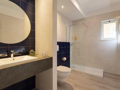 Bagno luminoso con specchio tondo, lavabo, doccia a filo pavimento e WC accanto.