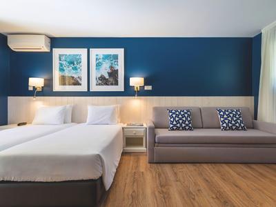 Camera moderna con due letti, divano, parete blu e pavimento in legno.