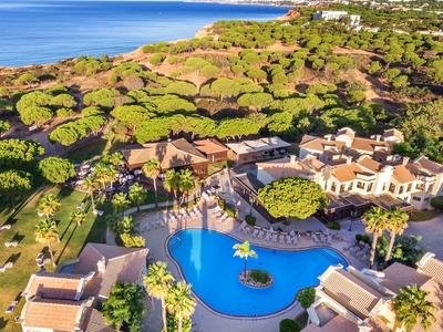 Complesso alberghiero di lusso con grande piscina, circondato da alberi verdi e vicino al mare.