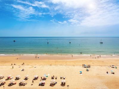 Ampia spiaggia di sabbia con lettini, poche persone e mare calmo sotto un cielo blu.