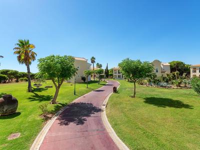 Red paved path through a green garden with trees and palms at a hotel resort.