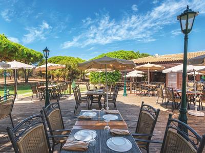 Terrazza soleggiata con tavoli apparecchiati e sedie sotto ombrelloni sotto un cielo azzurro.