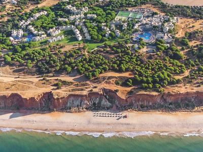 Vista aerea di un resort con piscine, alberi e spiaggia sabbiosa vicino al mare.