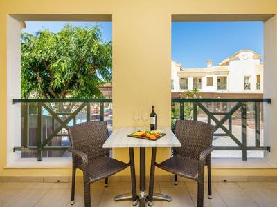 Balcone con tavolo, due sedie, bottiglia di vino, bicchiere e snack davanti a edificio e vegetazione.