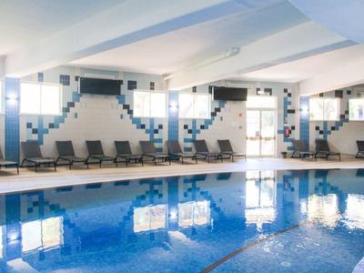 Piscina coperta con piastrelle blu, lettini e grandi finestre lungo la parete.