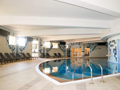 Area interna con piscina rotonda, sedie a sdraio e travi del soffitto bianche in un hotel.