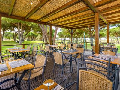 Überdachte Terrasse mit Tischen und Stühlen in einem grünen Hotelgarten.