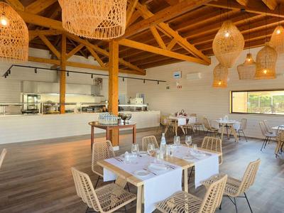 Modernes Restaurant mit Holzbalken, weißen Tischen und Stühlen sowie großen Lampen im Urlaubshotel.
