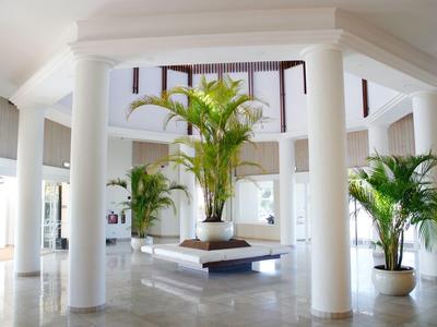 Helle Hotellobby mit weißen Säulen, glänzendem Boden und grünen Pflanzen als Dekoration.
