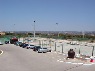 Large parking lot next to tennis courts in a rural setting under a clear blue sky.