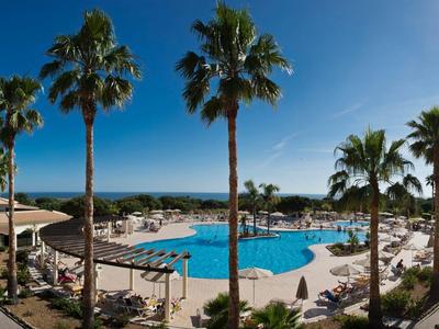 Grande piscina all'aperto con lettini e palme sotto un cielo azzurro sereno.