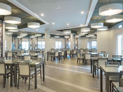 Ristorante d'hotel moderno e luminoso con molti tavoli e sedie dai colori neutri.