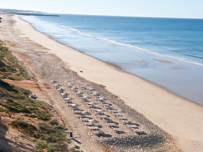 Lunga spiaggia di sabbia con lettini e mare blu sotto un cielo sereno.