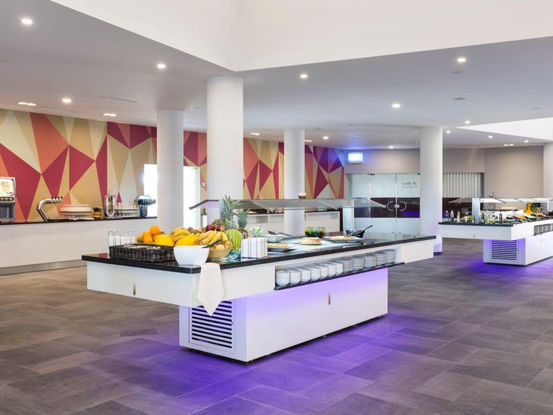 Sala da pranzo moderna in hotel con buffet, pareti chiare e decorazioni geometriche alle pareti.