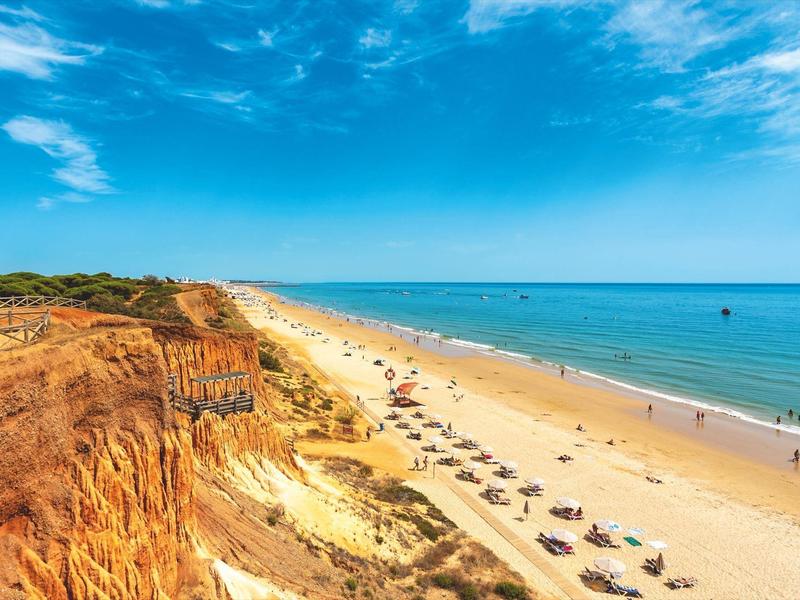 Vasta spiaggia con scogliere chiare, cielo blu e ombrelloni sul mare