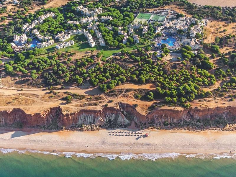 Vista aerea di un resort con piscine, alberi e spiaggia sabbiosa vicino al mare.