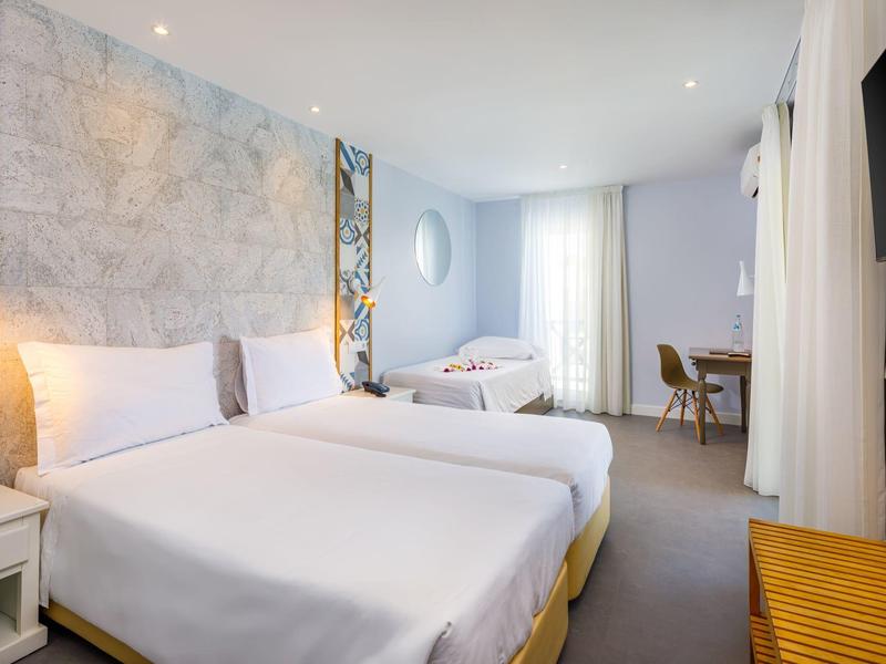 Camera d'hotel luminosa con due letti, scrivania, sedia e TV a muro.