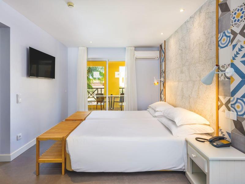 Camera d'albergo moderna con letto grande, TV e parete decorata colorata.