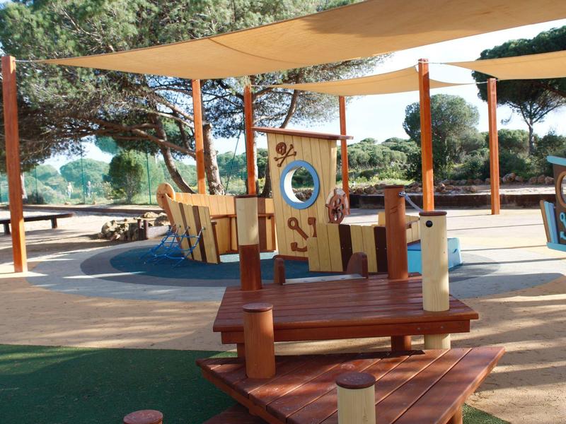 Parco giochi per bambini con strutture in legno e aree ombreggiate all'aperto