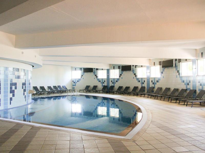 Piscina interna con lettini e ambiente luminoso in un hotel.