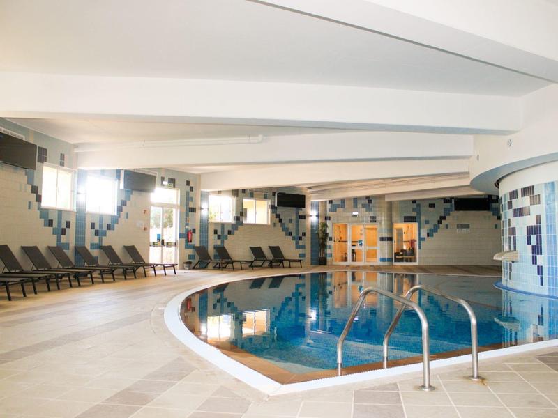 Area interna con piscina rotonda, sedie a sdraio e travi del soffitto bianche in un hotel.