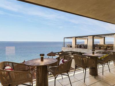 Moderner Außenbereich eines Hotels mit Sitzgelegenheiten und Blick auf das Meer unter blauem Himmel.
