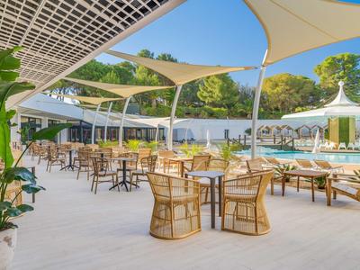 Area esterna moderna dell'hotel con posti a sedere all'ombra e vista sulla piscina.