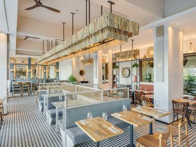 Caffetteria moderna con mobili in legno e metallo, grandi finestre e un lungo lampadario.