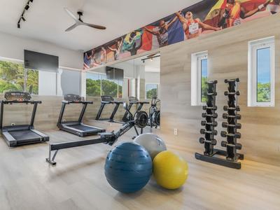 Moderne Fitnessraum mit Laufbändern, Hanteln, Gymnastikbällen und großen Fenstern mit Aussicht.