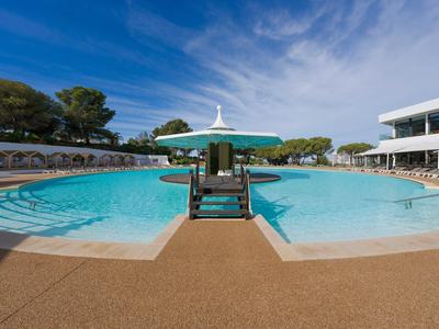 Grande piscina all'aperto con ombrelloni e lettini sotto un cielo azzurro in un hotel.