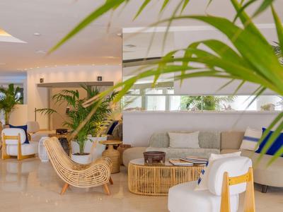 Area lounge dell'hotel luminosa e moderna con piante, mobili in vimini e posti a sedere.