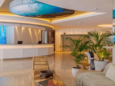 Moderna hall dell'hotel con banco reception, posti a sedere confortevoli e piante tropicali.