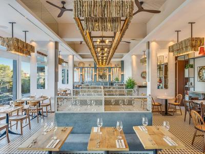 Helles Restaurant mit Holztischen, grauen Sitzbänken, großen Fenstern und Bambus-Deckenlampen.